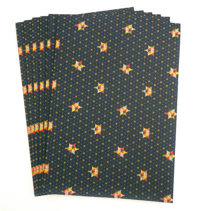 Stack of folded wrapping paper sheets with geometric star pattern on a dark blue background