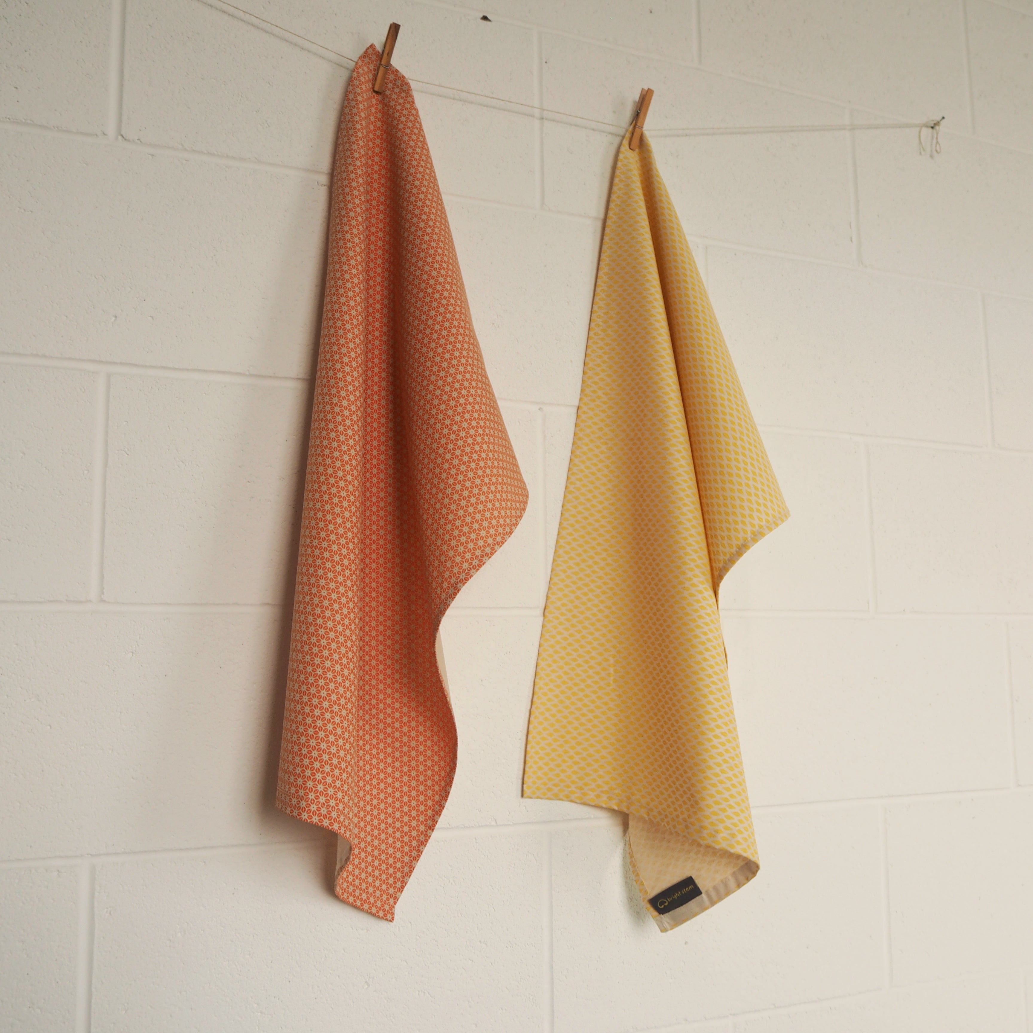 two bright stem tea towels with yellow triangle and orange star pattern printed with water based ink on organic cotton