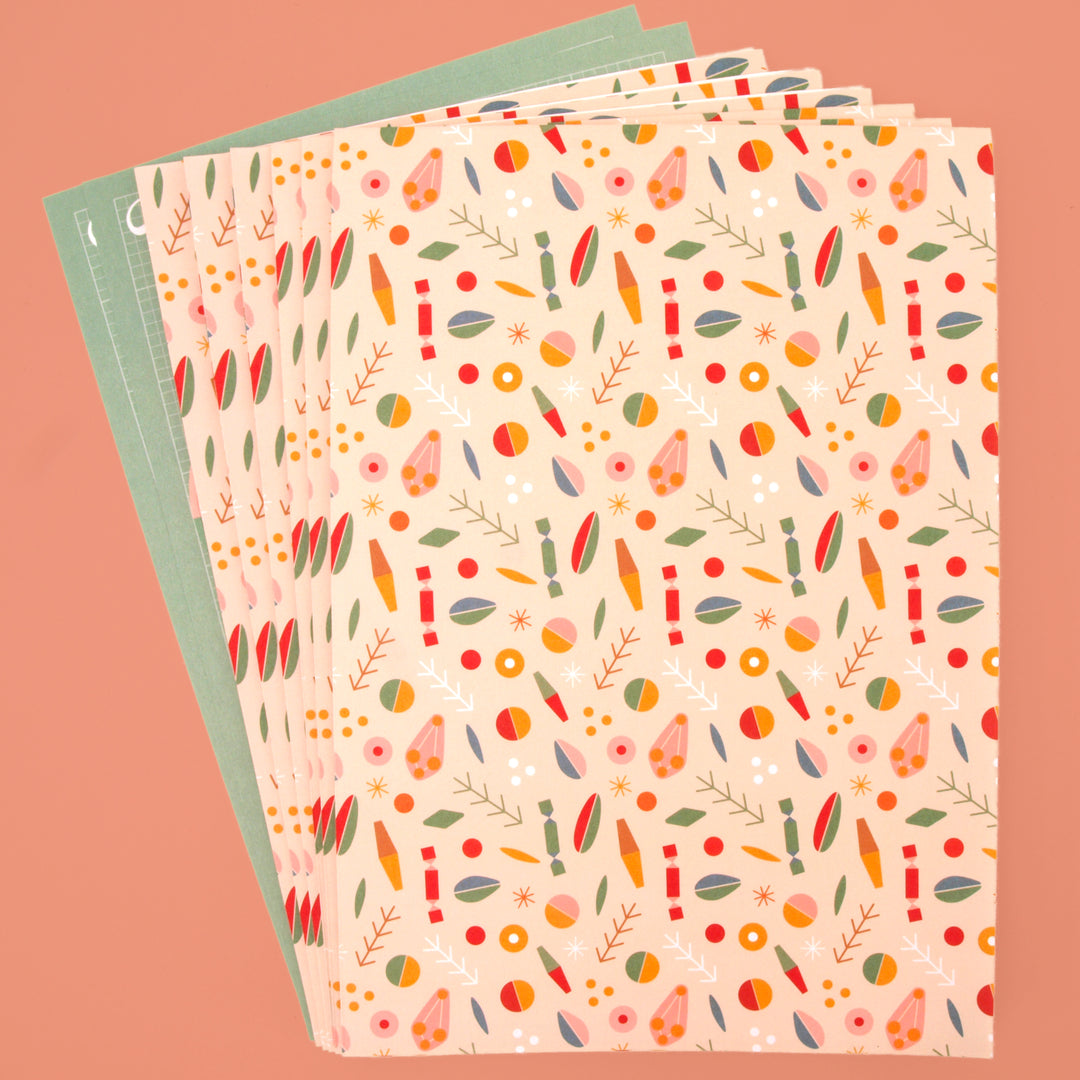 Six sheets of recyclable wrapping paper folded and two sheets of pop out tags displayed on a pink background.