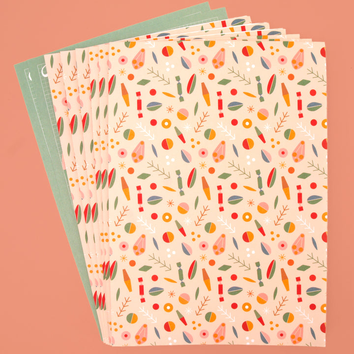 Six sheets of recyclable wrapping paper folded and two sheets of pop out tags displayed on a pink background.