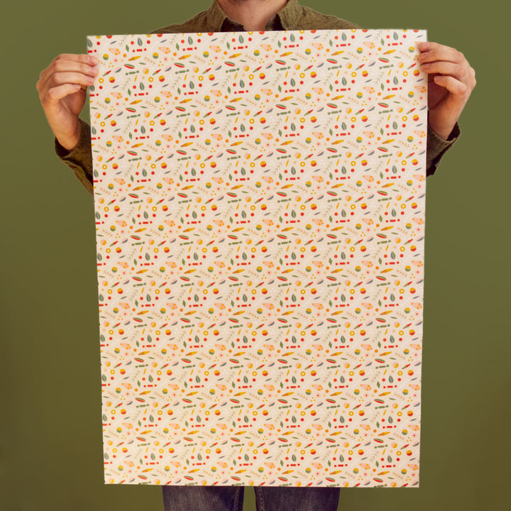 Artist holding a large sheet of Christmas wrapping paper with a colourful pattern against a green background. 