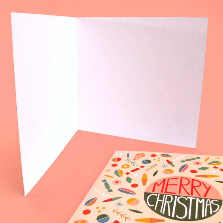 Open Christmas card, blank inside ready for your personal festive  message. with a colourful 'Merry Christmas' card  at bottom. on a pink background