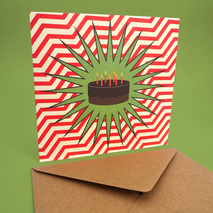 Birthday Card with chocolate cake and candles in the style of a comic book or POP Art  design on a red and white zigzag pattern, with a brown Kraft envelope.