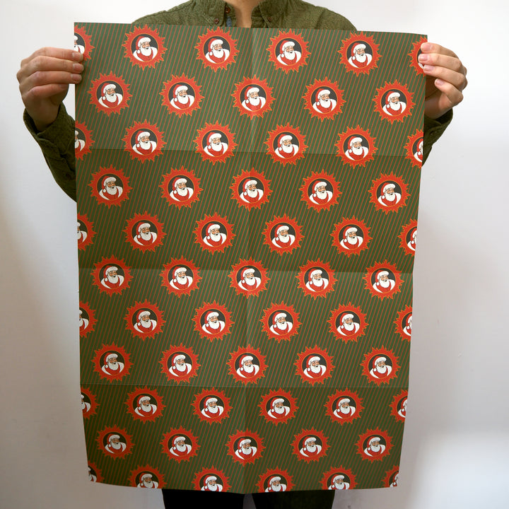 Artist holding a large sheet of bright stem wrapping paper with red and white Santa designs on a green background.
