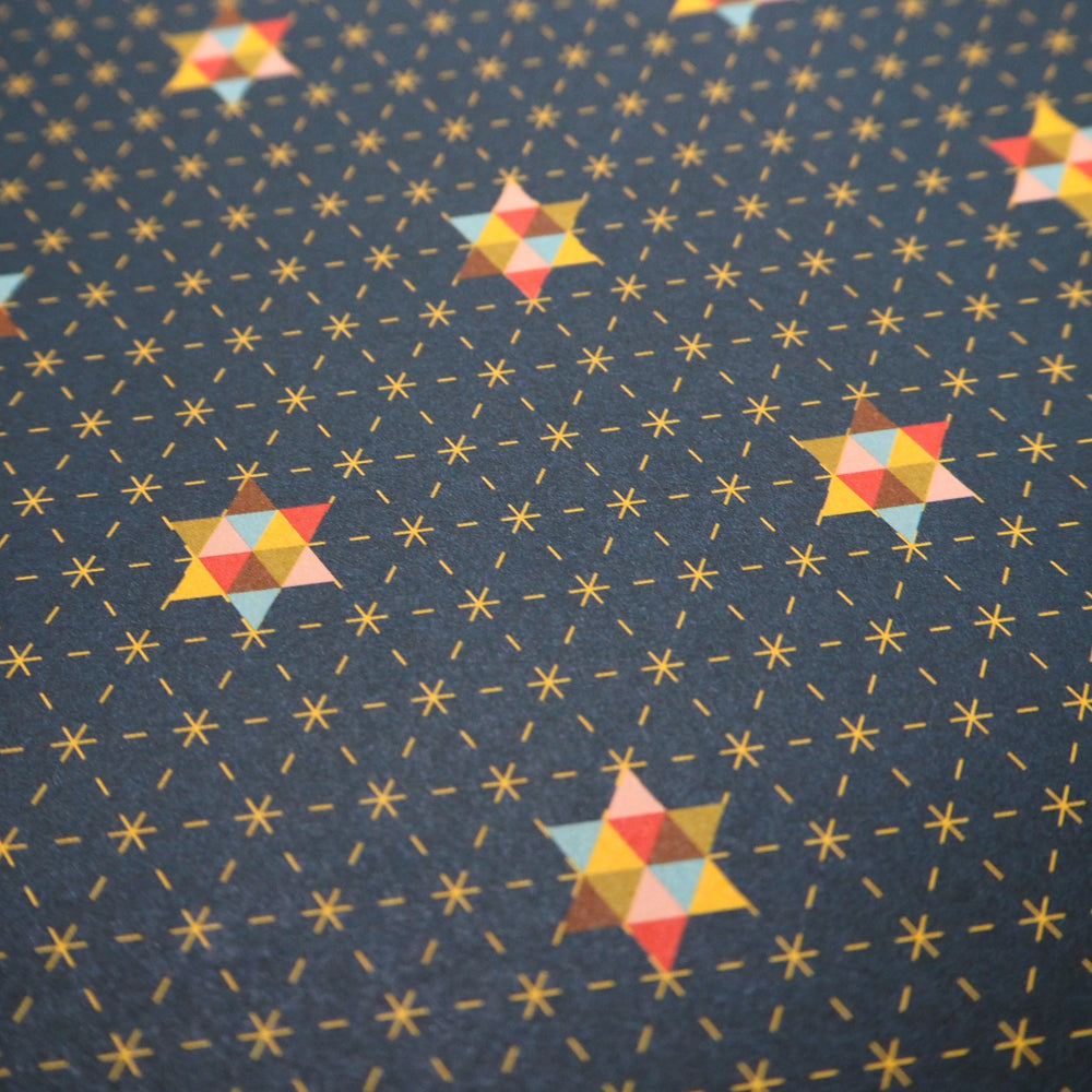 close up photo of Bright Stem Patterned Christmas wrapping paper with colourful star designs on a blue background with tiny yellow stars