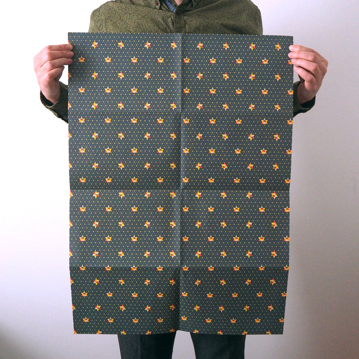 Artist holding a sheet of Christmas wrapping paper he designed with a pattern of small multicoloured stars on a blue background.
