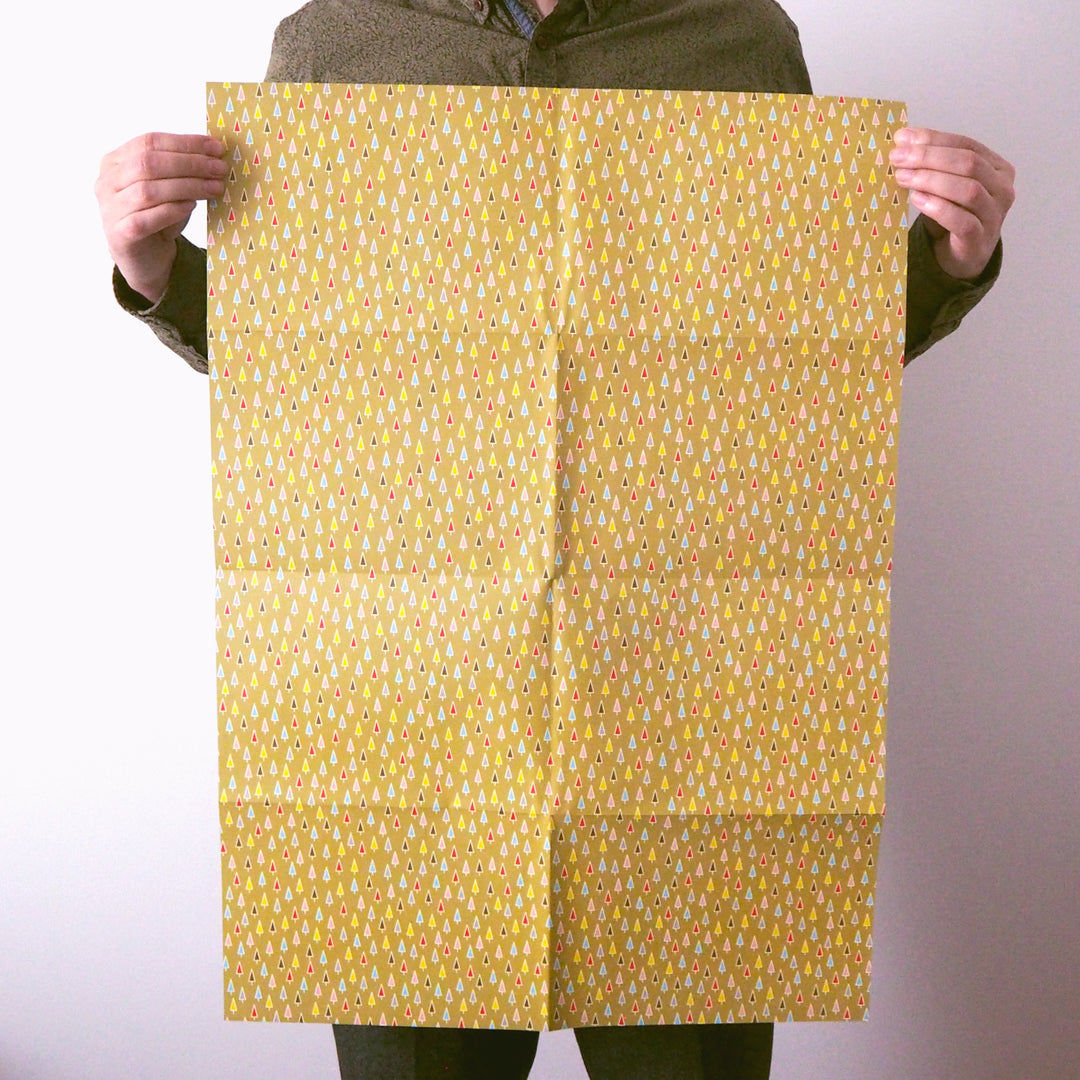 Sheet of Bright Stem Recyclable Christmas Wrapping Paper Gift Wrap. Multicoloured Christmas Trees on a light green background. Held by Artist