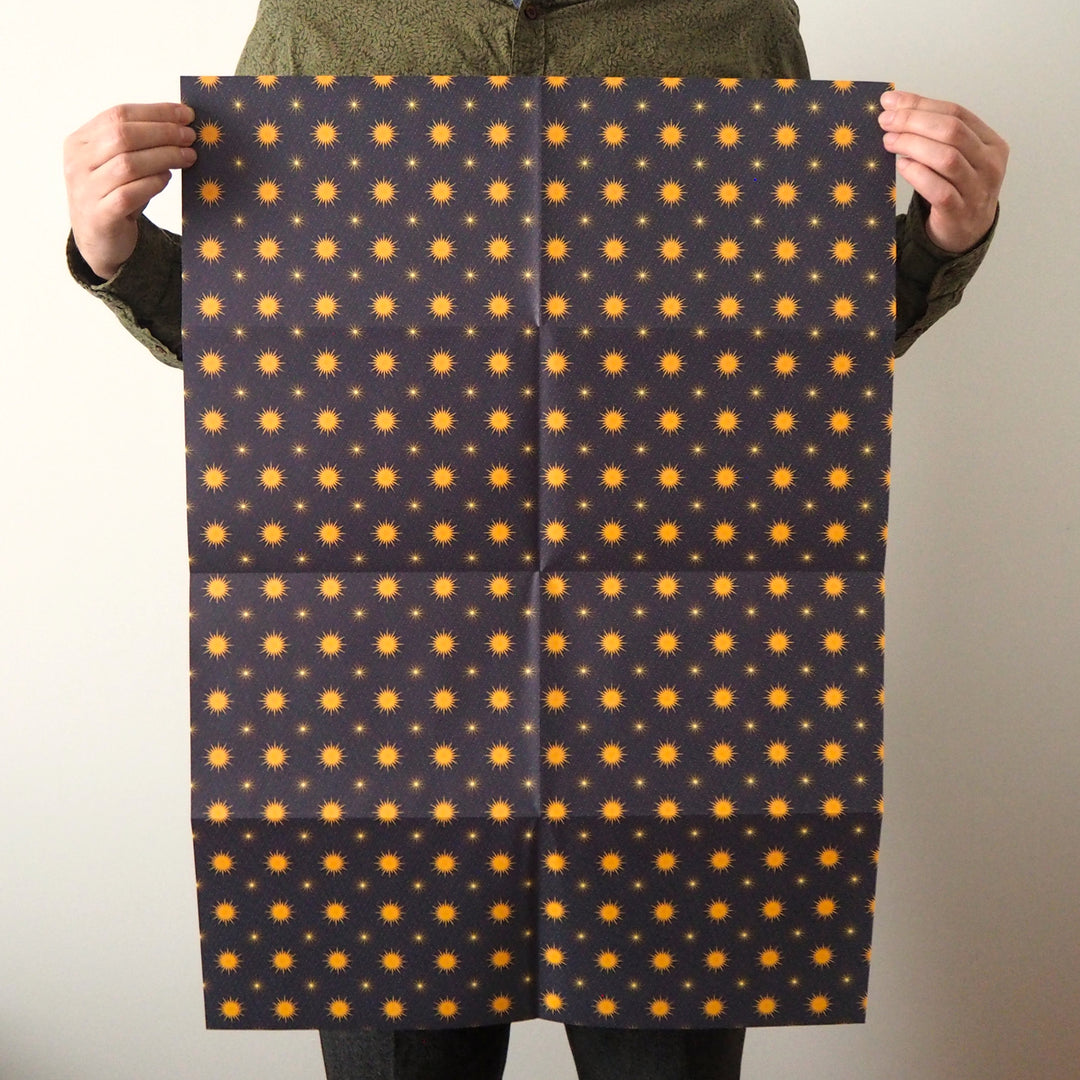 Bright Stem Recyclable Christmas Wrapping Paper Gift Wrap. Yellow star pattern on a dark blue background held by artist.