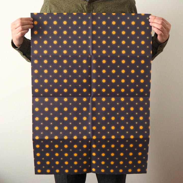 Bright Stem Recyclable Christmas Wrapping Paper Gift Wrap. Yellow star pattern on a dark blue background held by artist.