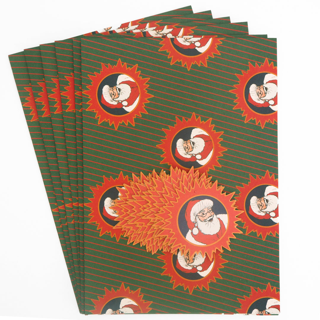Stack of 6 green and red recyclable  christmas wrapping paper with Santa Claus design printed on. And 12 Christmas tags with Santa on. From Bright Stem