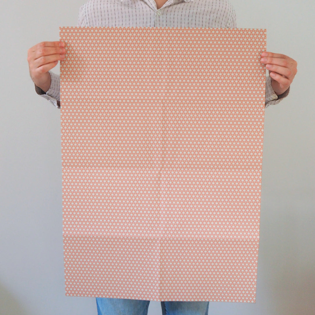 Artist holding a sheet of recyclable wrapping paper with a subtle orange star pattern against a plain background