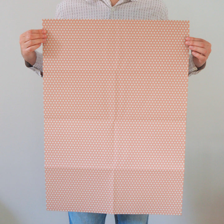Artist holding a sheet of recyclable wrapping paper with a subtle orange star pattern against a plain background