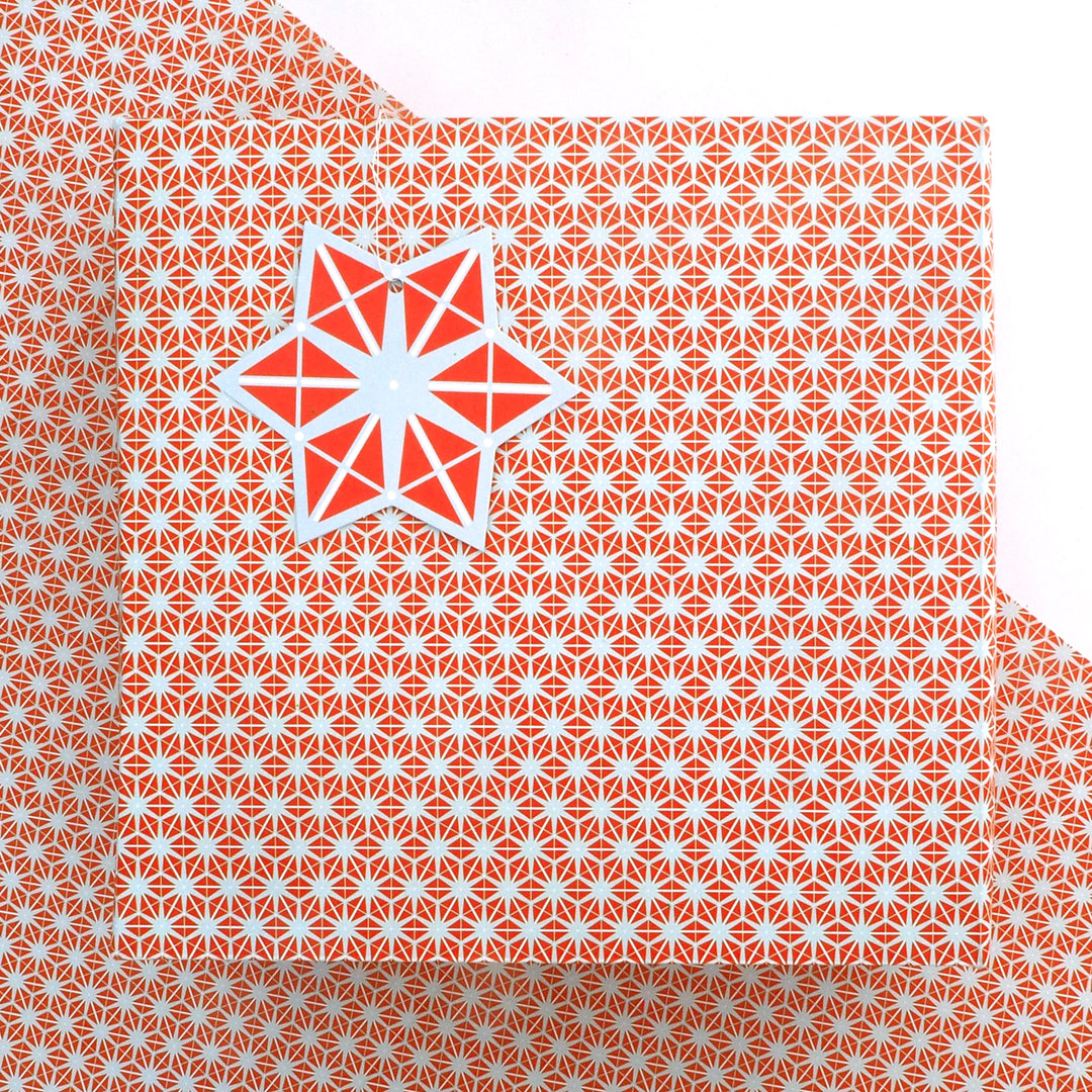 recyclable wrapping paper featuring an orange and grey geometric star pattern  with a matching tag on a matching background