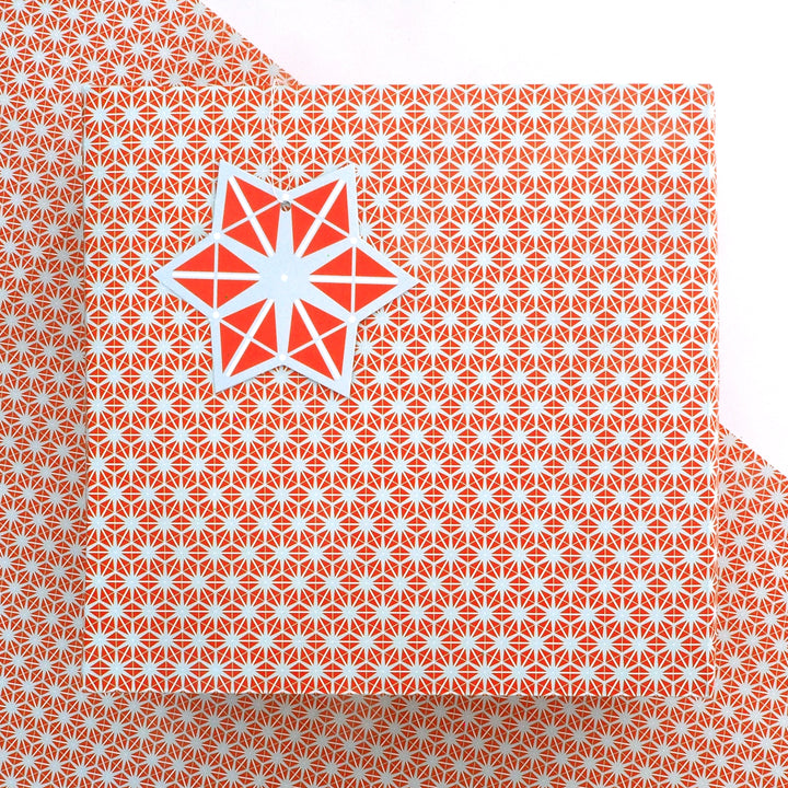 recyclable wrapping paper featuring an orange and grey geometric star pattern  with a matching tag on a matching background