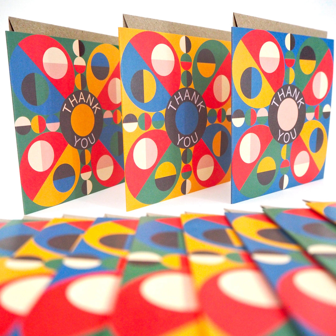 Express your gratitude with these striking modern thank you cards featuring bold geometric designs from Bright Stem. Sold by the Artist. Each set includes 12 cards with three unique patterns (4 of each design) accompanied by matching recycled brown paper envelopes. The vibrant colour palette combines rich reds, blues, greens, and yellows in an eye-catching circular motif, with each design centred around a distinctive 'Thank You' message. Measuring 12 x 12 cm