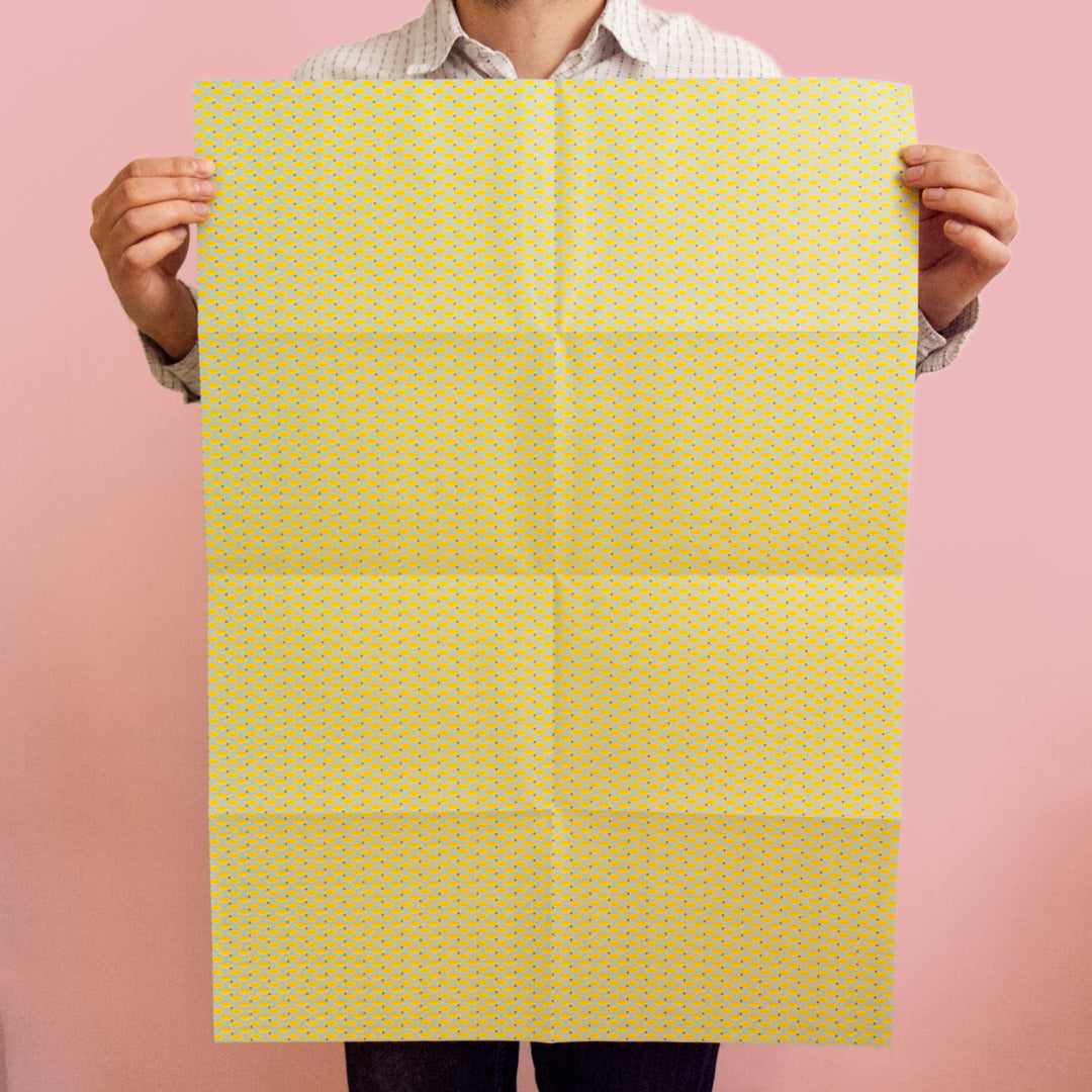 Bright Stem recyclable wrapping paper sheet held by artist/designer. Geometric yellow diamond  pattern on blue. 50x70cm made in the UK