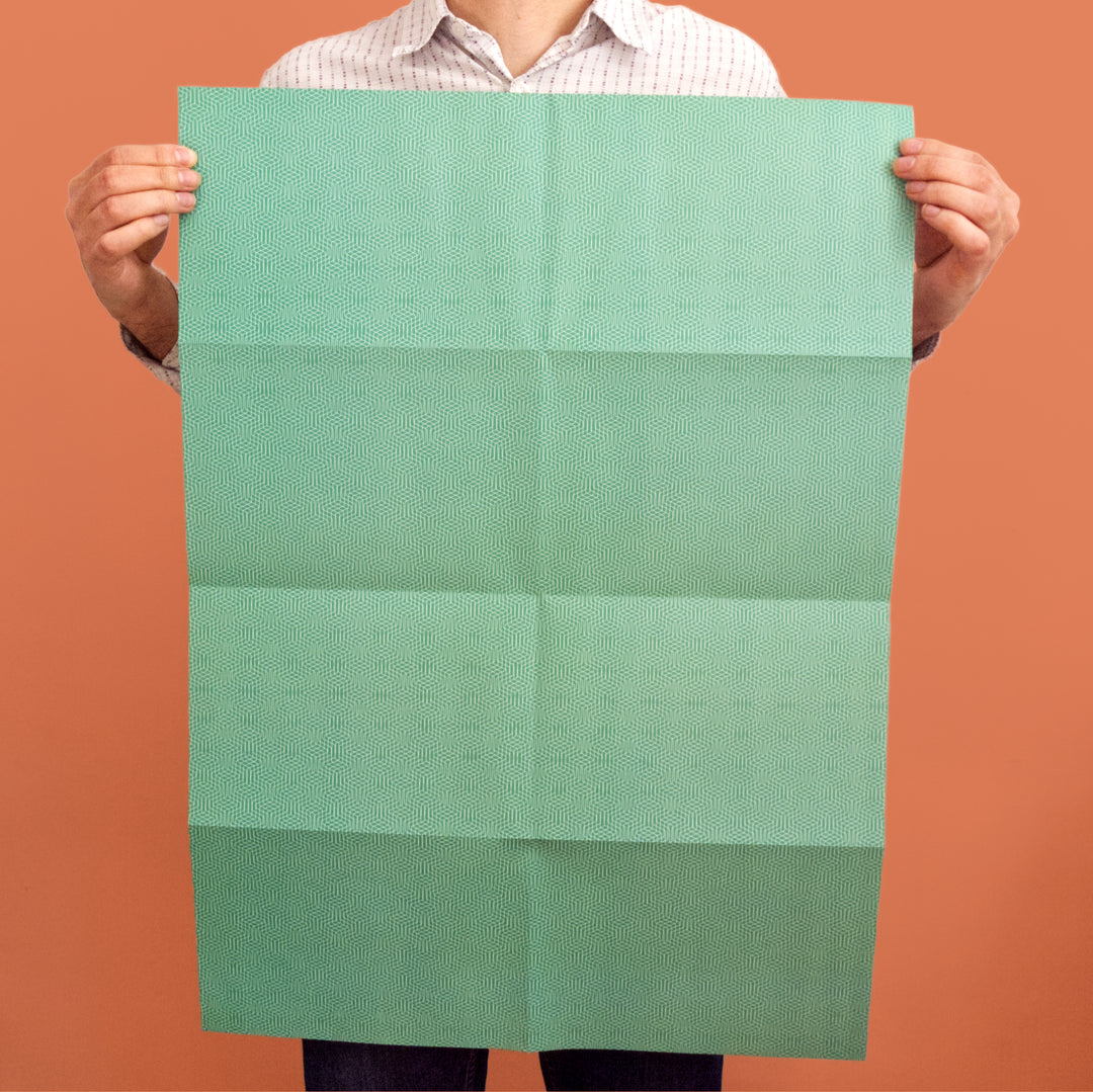 Bright Stem recyclable wrapping paper sheet held by artist/designer. Emerald green geometric zig zag pattern. 