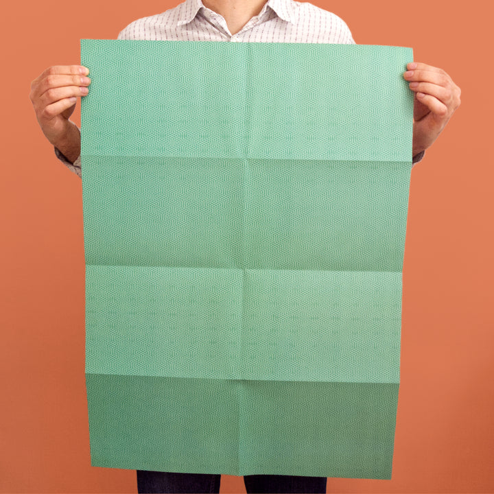 Bright Stem recyclable wrapping paper sheet held by artist/designer. Emerald green geometric zig zag pattern. 