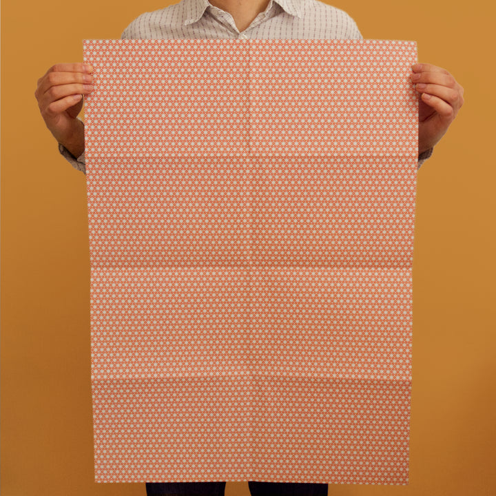Bright Stem recyclable wrapping paper sheet held by artist/designer. orange/red and grey star pattern. 50x70cm