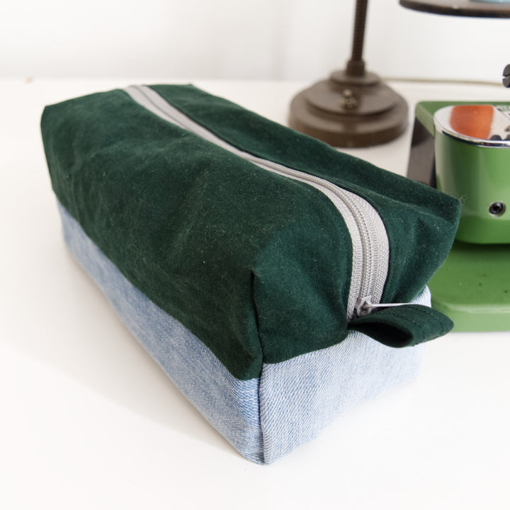 Bright Stem wash bag made from green cotton and light blue denim upcycled fabric  with a grey zipper.. Next to a vintage sewing machine.