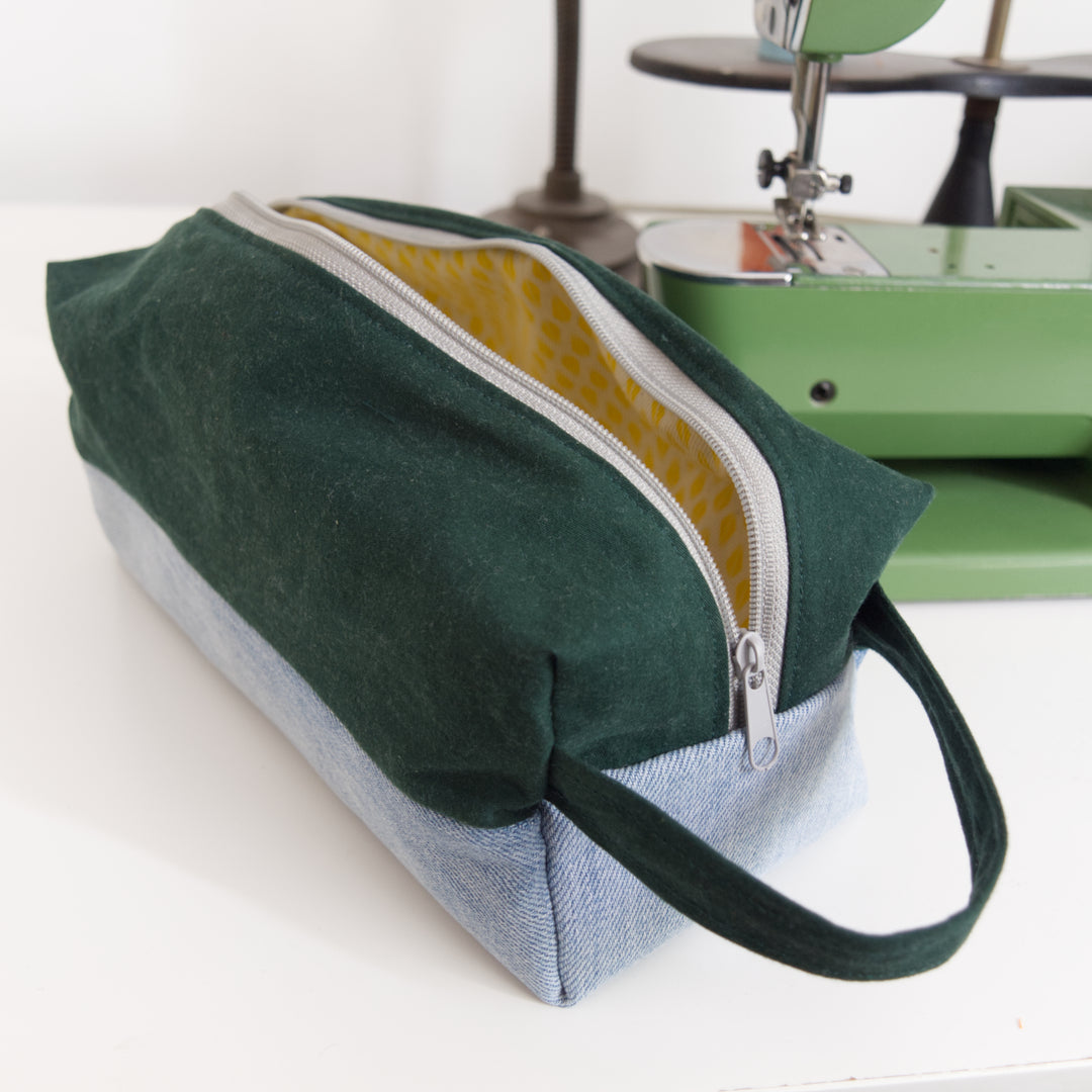 Bright Stem wash bag made from green cotton and light blue denim upcycled fabric with a yellow and white cotton inner lining with grey zipper. Next to a vintage sewing machine.