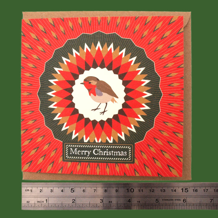 Christmas card with a robin design and 'Merry Christmas' text on a red and bronze kaleidoscopic pattern. Accompanied by a ruler for size reference.