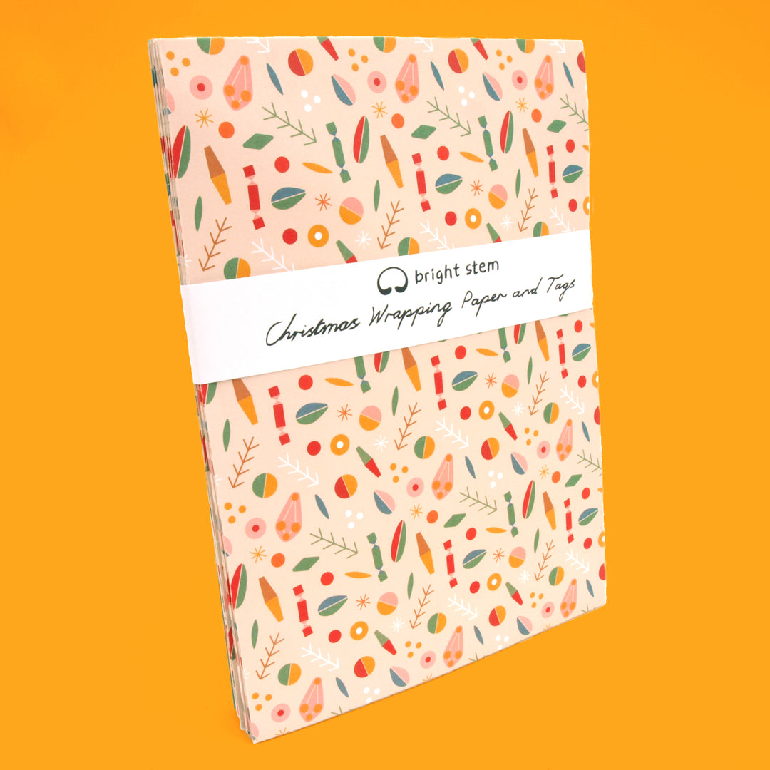 Pack of recyclable Christmas wrapping paper with colourful patterns wrapped in a bright stem branded belly band against a yellow background.