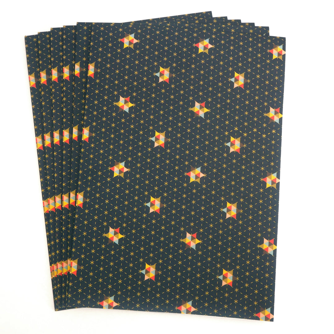 Stack of folded wrapping paper sheets with geometric star pattern on a dark blue background