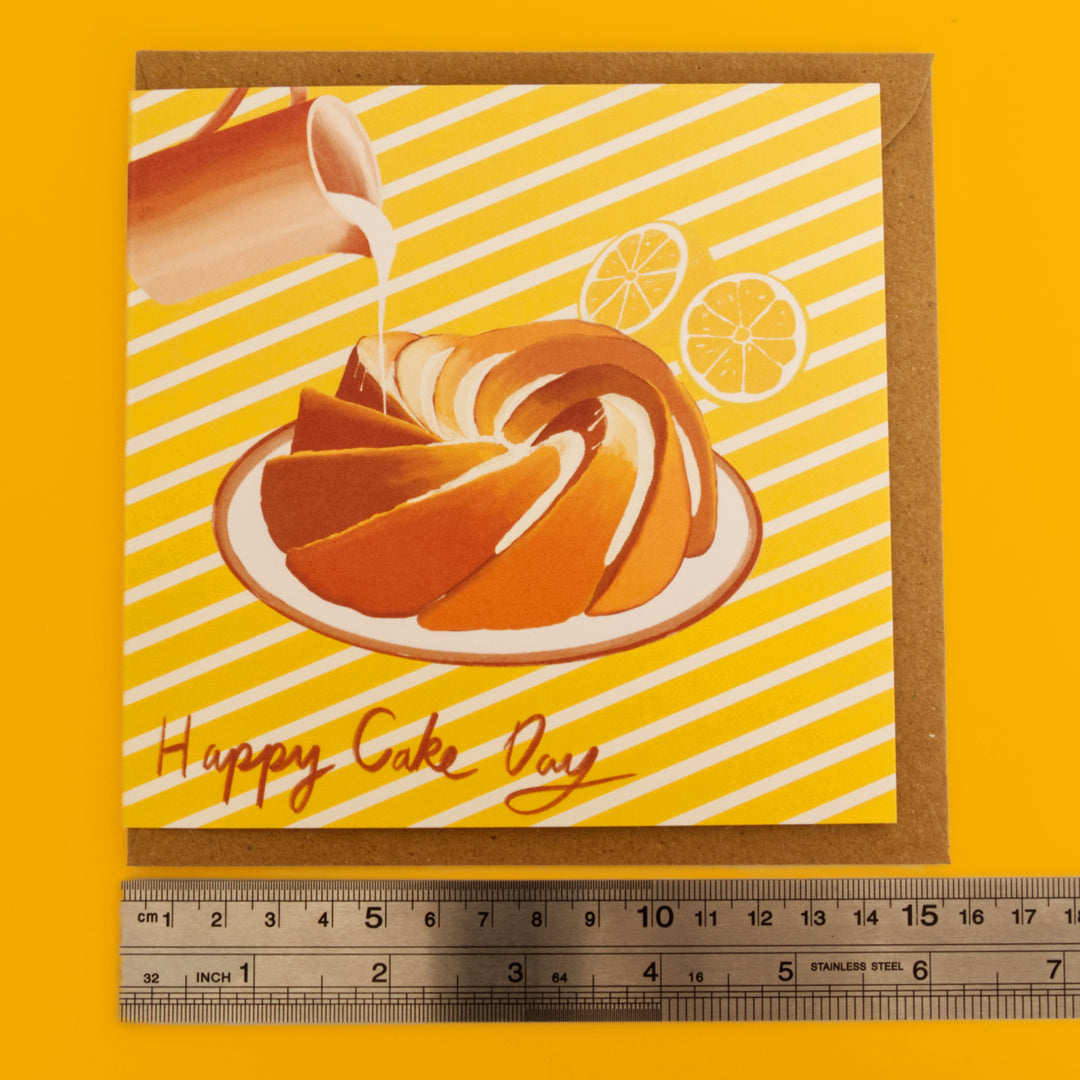 Illustration of a bundt cake with lemon slices and a drizzle on a yellow background with 'Happy Cake Day' text. Ruler bellow to show the length of cards and envelopes