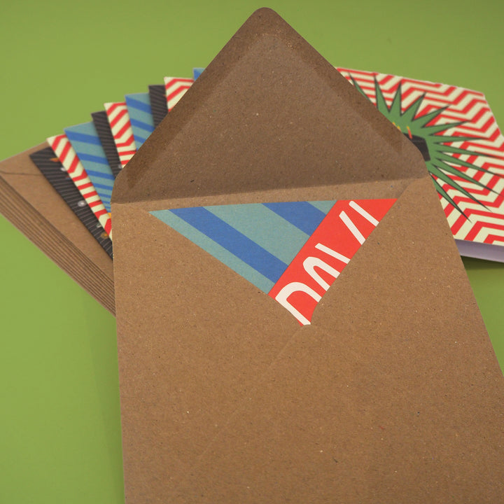 Brown envelope with colorful bright stem birthday card inside. With a stack of birthday cards and envelopes behind all on a green background