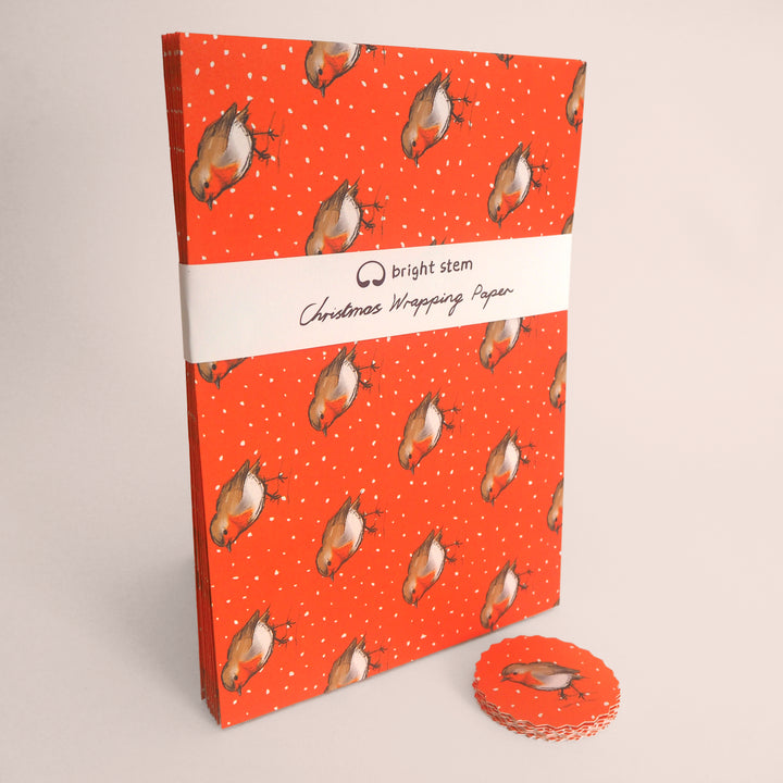 Pack of Bright Stem Recyclable Christmas wrapping paper with an illustration of a Robin on an orange background. With a stack of matching tags bellow