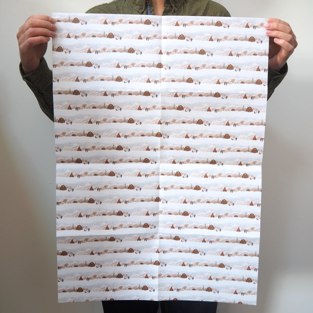 Artist holding a large sheet of bright stem wrapping paper with illustrations of snow covered landscape.