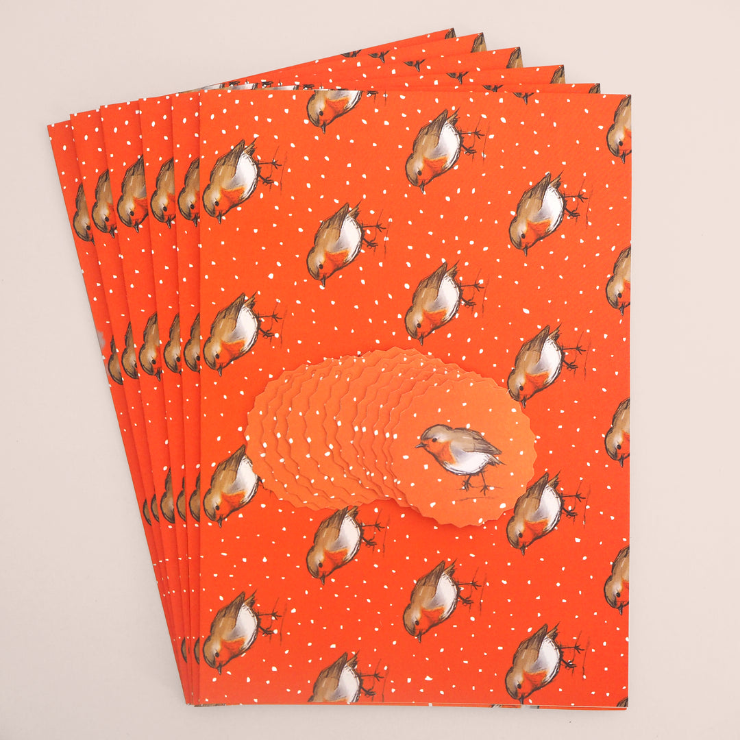 Stack of 6 folded sheets of orange recyclable Christmas wrapping paper with robin illustration printed on. And 12 Christmas tags also with robin illustration on. From Bright Stem