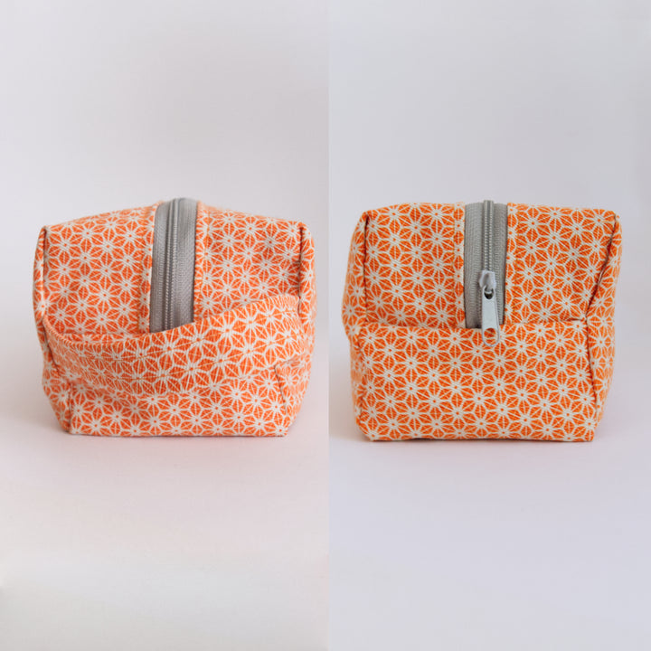 Two views of an orange and grey patterned bright stem wash bag with a gray zipper on a white background. Handmade by the Artist