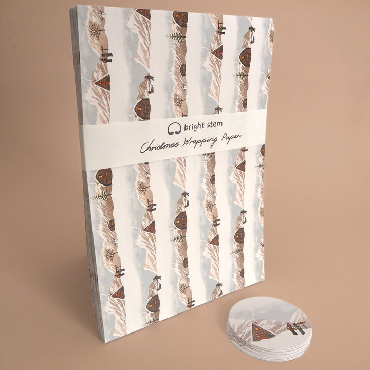 Pack of Bright Stem Recyclable Christmas wrapping paper with an illustration of a Winter Landscape. With a stack of matching tags bellow