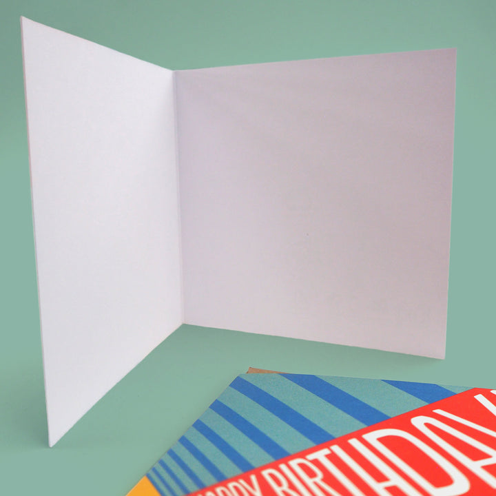 Open birthday card with blank inside ready for your personal birthday message. with a colourful 'Happy Birthday' card and envelope at bottom. on a green background