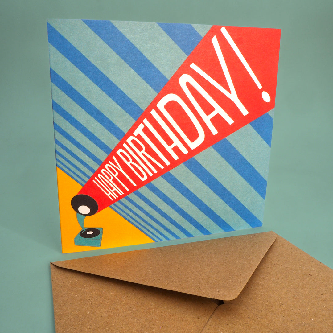 Colourful birthday card with 'Happy Birthday!' text and a record player graphic, accompanied by a brown envelope on a green background. Inspired by the Bauhaus graphic design 