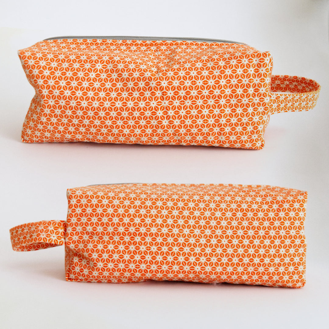 Two views from right hand side and left hand side of bright stem orange patterned toiletry bag on a white background