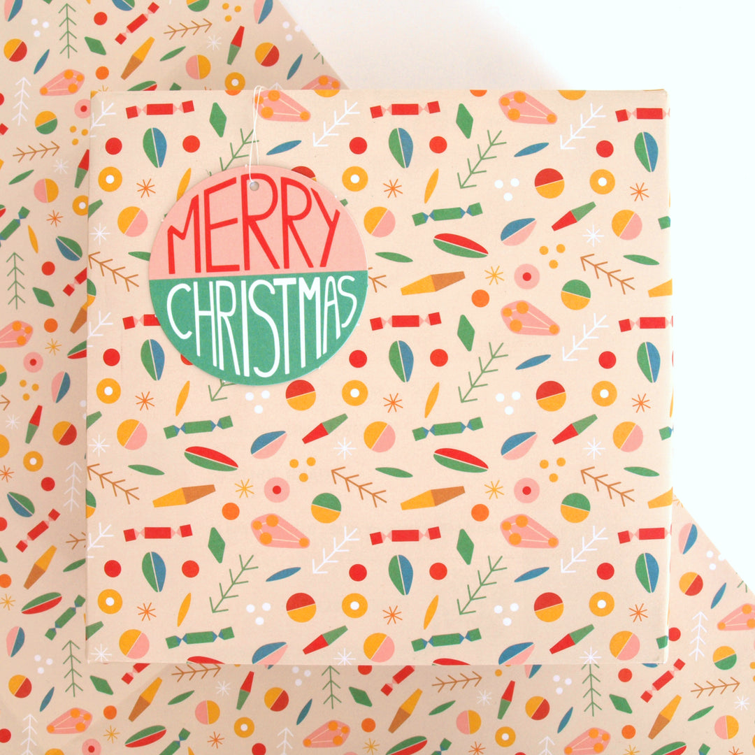 Present wrapped in Recyclable Christmas wrapping paper with abstract geometric patterned on a cream background with 'Merry Christmas' text on a swing tag.