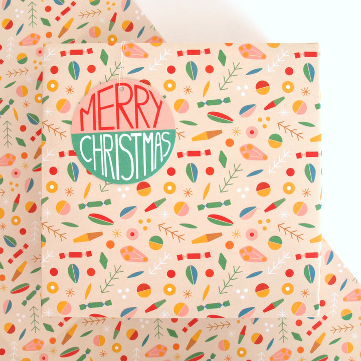 Present wrapped in Recyclable Christmas wrapping paper with abstract geometric patterned on a cream background with 'Merry Christmas' text on a swing tag.