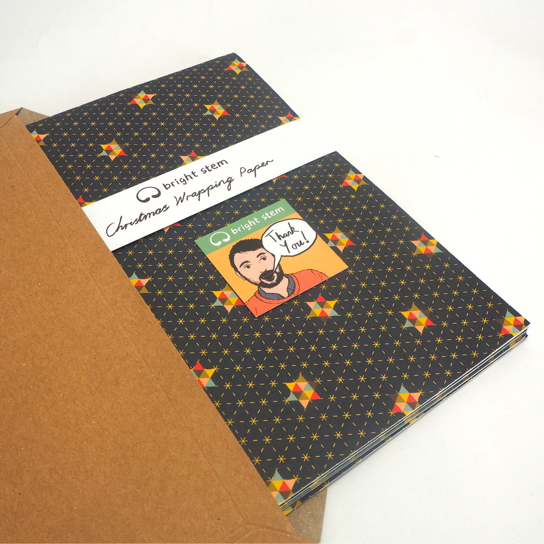 Stack of  bright stem Christmas wrapping paper with a thank you card from the artist. being packed in envelope