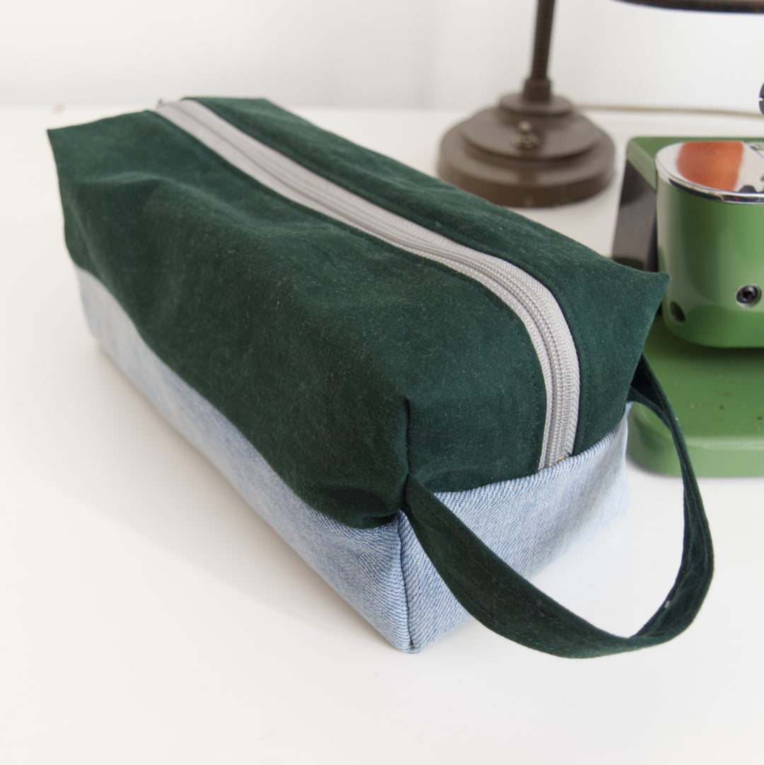 Bright Stem wash bag made from green cotton and light blue denim upcycled fabric  with a grey zipper.. Next to a vintage sewing machine.