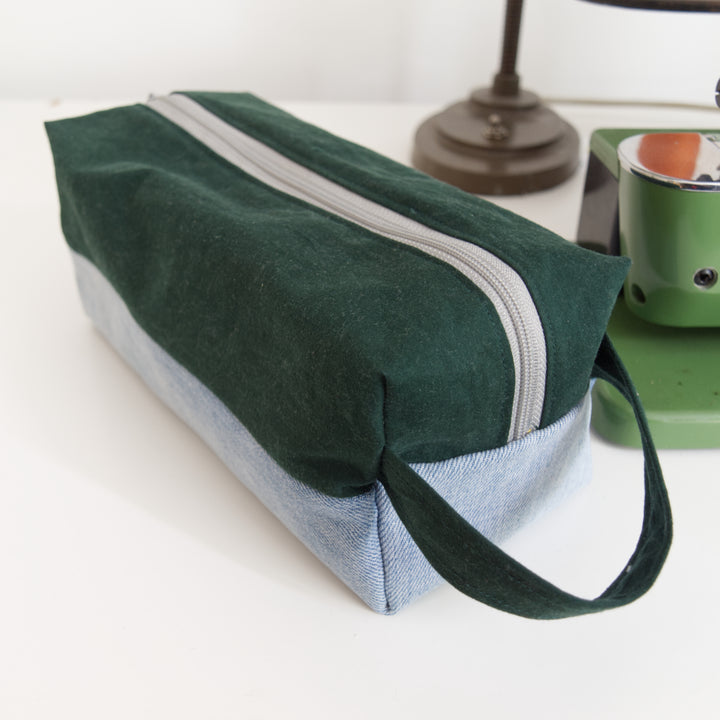 Bright Stem wash bag made from green cotton and light blue denim upcycled fabric  with a grey zipper.. Next to a vintage sewing machine.
