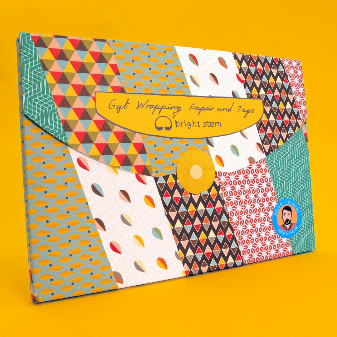 Plastic free packaging. A folder containing bright stem gift wrapping paper showing various geometric patterns. Displayed on a yellow background