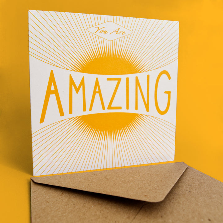 Bright Stem congratulations card. Featuring a warm vintage-style sun illustration and the uplifting message "You Are Amazing," stud upright with brown Kraft envelope in front.  