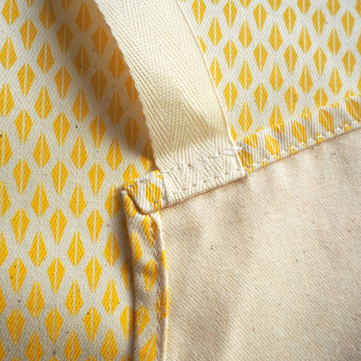 Bright Stem apron close up detail image of   back of apron showing strap attached to seam. With yellow triangle pattern behind.