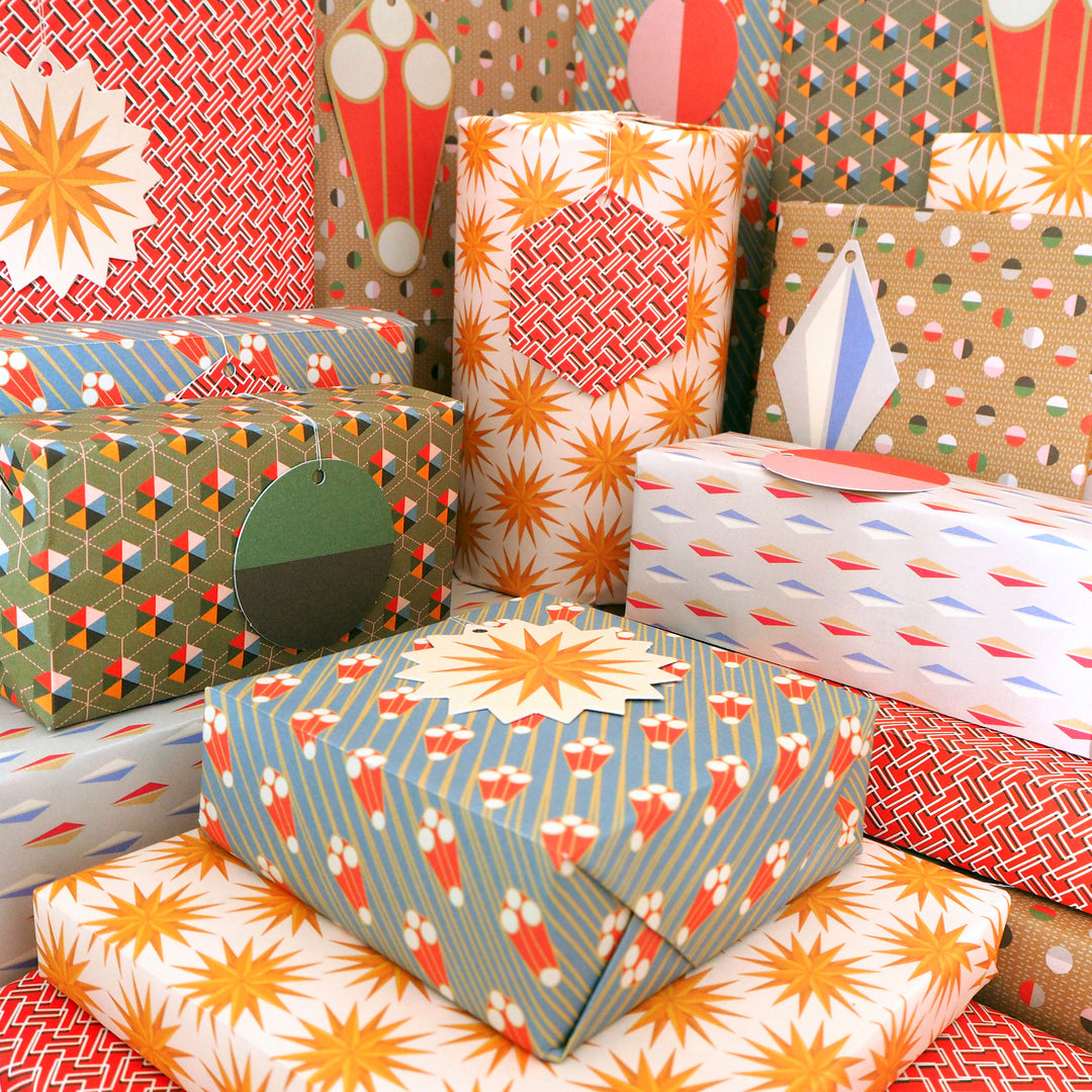 bright stem gift-wrapped presents with tags. Recyclable Gift Wrapping Paper Geometric unique multicoloured designs Vintage Style Patterns. Stars sculptures, triangles hexigans. early 20th century, modernist, art deco style designs, ethically manufactured, made in the uk, recycled sustainable